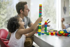A family sits at a table and a little girl with special needs plays with building blocks. Trusts can be established at any age. 